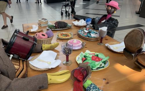anthropomorphized thrifted objects that look like people sitting around a table with hand-crafted fake food 