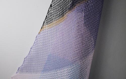 Knitted yarn hung in the shape of a sail boats sail. The yarn is purple, black, white and gold. 