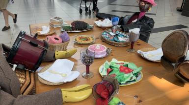 anthropomorphized thrifted objects that look like people sitting around a table with hand-crafted fake food 