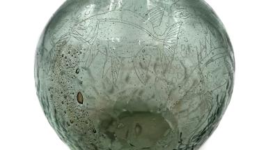 a circular glass vase etches with fish and other botanicals with a green hue