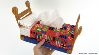 a hand holding a cross stitched tissue box that looks like a bed with text on either side of the image that reads "Big Absence" and "Small Presence" in handwritten text