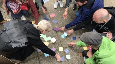 Group of people kneeling around several colourful post-it notes on a sidewalk