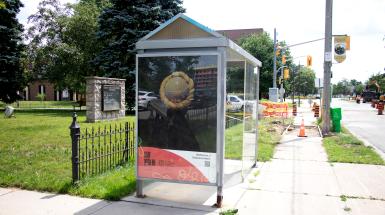 The back of a head of a yellow headwrap on a black background, mounted in an advertisement slot at a bus stop.