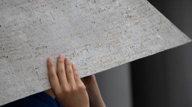 Hands grasping a grey pyramid hat covered in names.
