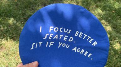 A round blue cushion that says "I focus better seated. Sit if you agree."