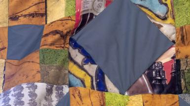 Closeup of the quilt. There are patches of grey reflective material mixed with other unknown images of texture and objects.