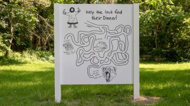 A billboard with a squiggled maze leading from an Inuk holding utensils to a bear dead end, junk food dead end, and a fresh goose in the centre as a finish. 