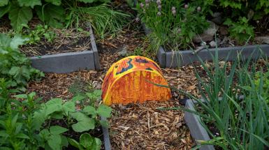 A bright yellow and orange semicircle at a crossroads made by four slightly raised garden beds and wood chip paths.