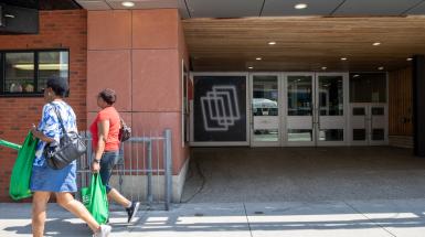 Further back view of the vinyl installed on its window by the doors of THE MUSEUM. Two people are walking by.