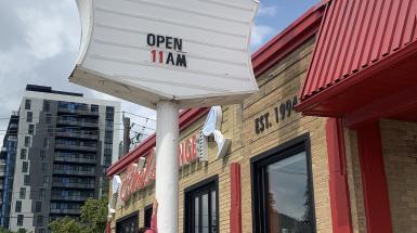 The artist is posing with the tall sign for the restaurant Ethel's.