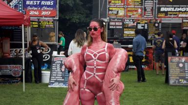 The artist is posing in front of BBQ stands at Ribfest.