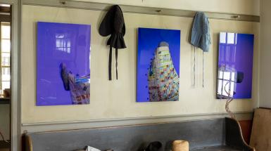 Acrylic panels with blue/indigo background among historical house items, depicting the artist wearing and interacting with their teabag quilt.