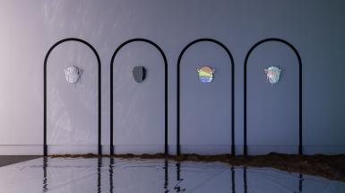 Four masks made of mirror pieces each in the centre of an arch, reflecting the nearby projected video screen. There is sand built up on the floor at the edges.