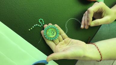 An open hand holding out a beaded Protect the Tract badge, all tinted green by incoming light.