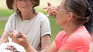 Three people sitting at a picnic table sculpting clay while talking.