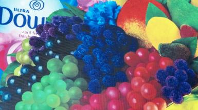 Closeup of bright colourful items arranged in still life - a rainbow of coloured grapes, other fake fruits, a bottle of Downy fabric softener