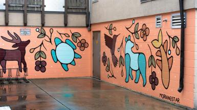 Mural with colour pallet that uses orange, turquoise, and browns. Mural depicts different wild life and plants. Such as a caribou, bear, turtle, humming bird, and fish.  