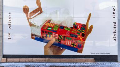 poster of hand holding cross stitched bed shaped tissue box cover. And text that reads big absence, small presence.  