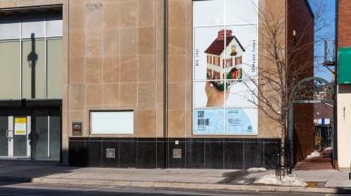poster of hand holding cross stitched house shaped tissue box cover. And text that reads big loss, small softness.