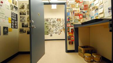 A small room with door open. all walls are cover with various give artifacts (like photos and cards) and organized neatly.