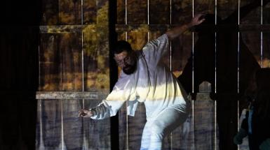 Artist with arms spread, in front of a fence.