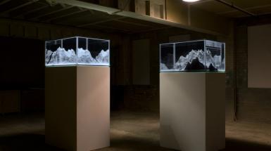 Image of two plinths with glass cases on top which hold models of mountains.