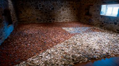 A brick room filled with broken tiles on the floor. There are two colours of tile white and red that are laid out in a geometric pattern.