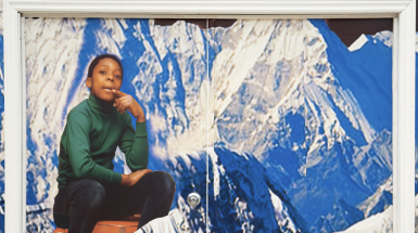 A large collage of young black boy sitting cross legged in front of large mountains.