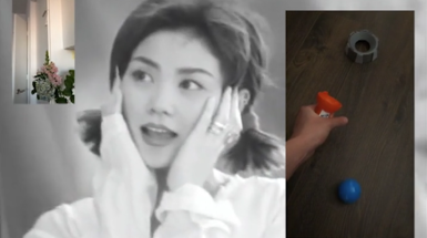 Screen shot of Video. Black and white image of woman in the Bckground holding her face. Image in foreground on left shows a plant in a room. Image in foreground on right shows hand playing with toy.
