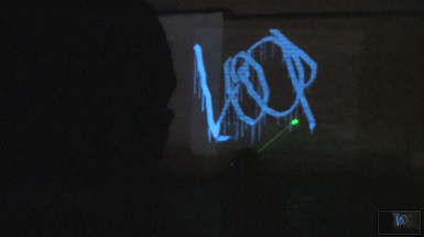 man using laser to draw projected graffiti that says "loop"
