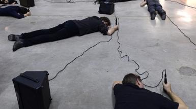 multiple men lying on the floor holding microphones which are pointing at the floor. 