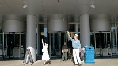Three figures, an old man and young girl point to the sky. Young boy stands behind them.