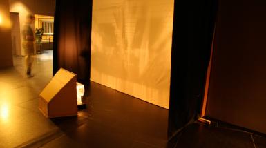 A projector in a cardboard structure shinning through a translucent box on to a screen. 