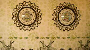 Two circular frames with art inside on top of intricate wallpaper that features insects.