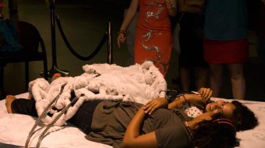 Two woman lying on bed with blanket that has wires coming from it. 