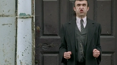 Still from John Duffy's Brother. Man with face of frustration who looks to be blowing air with hands at his side in fists. 