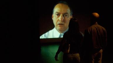 a couple standing in front of a projection of a man speaking.