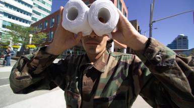 Person in military attire looking through two toilet paper rolls like binoculars 