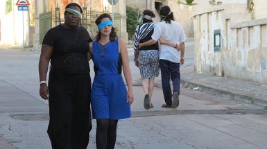 Two individuals walking down a street with each having one eye covered by a blind fold
