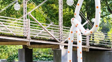 Image of sculpture of large polkadot rope emerging from river and tied in a knot