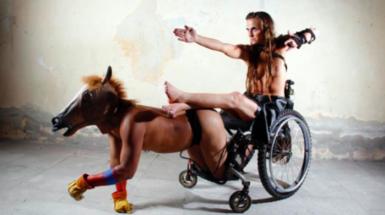 Image of man in wheel chair being pulled by man on all fours in horse mask