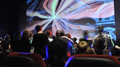image of people gathering in theatre as abstract lines and colours are projected