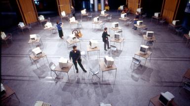 room filled with tables and chairs set up in circles which has desktop computers on top