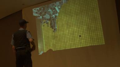 Visitor looking at projection of yellow grid with the top left corner a birds eye view of a city scape.