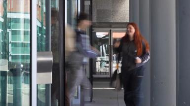 Two individuals walking through revolving door. 
