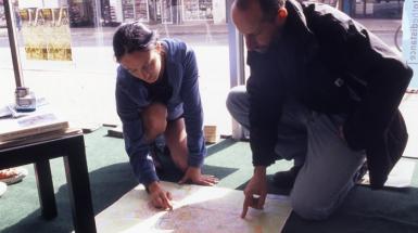 two people crouched pointing at map on floor