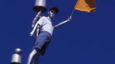Sculpture of boy holding yellow flag atop a flag pole