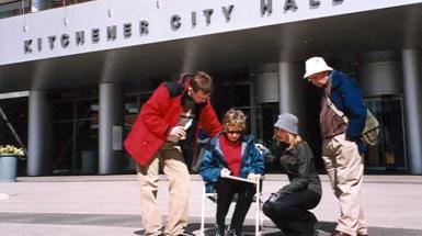 Three people looking over a figure sitting in chair drawing