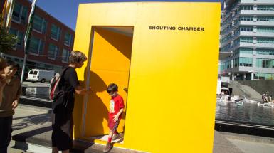 A young boy coming out of yellow box/room that says shouting chamber