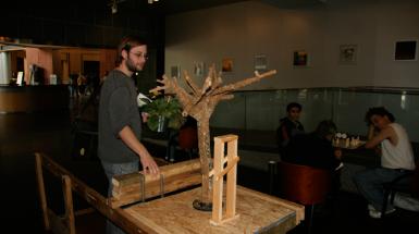 Man interacting with sculpture which features a small leafless tree